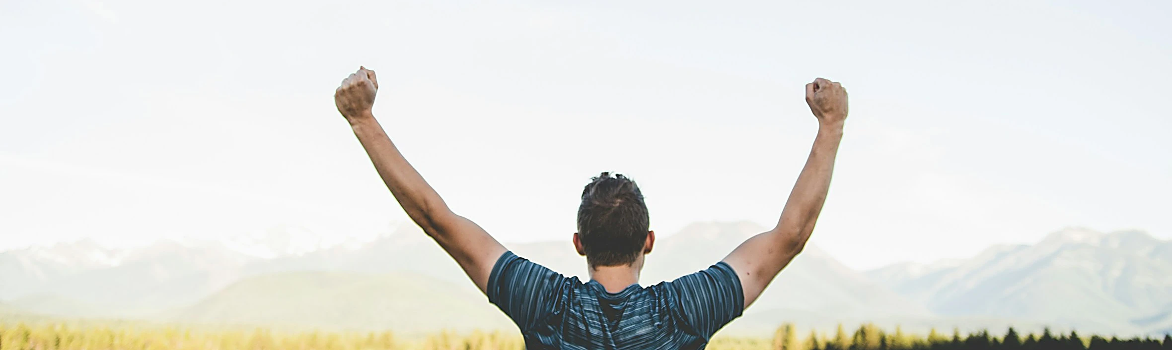 Man with raised arms facing a mountain field, celebrating
